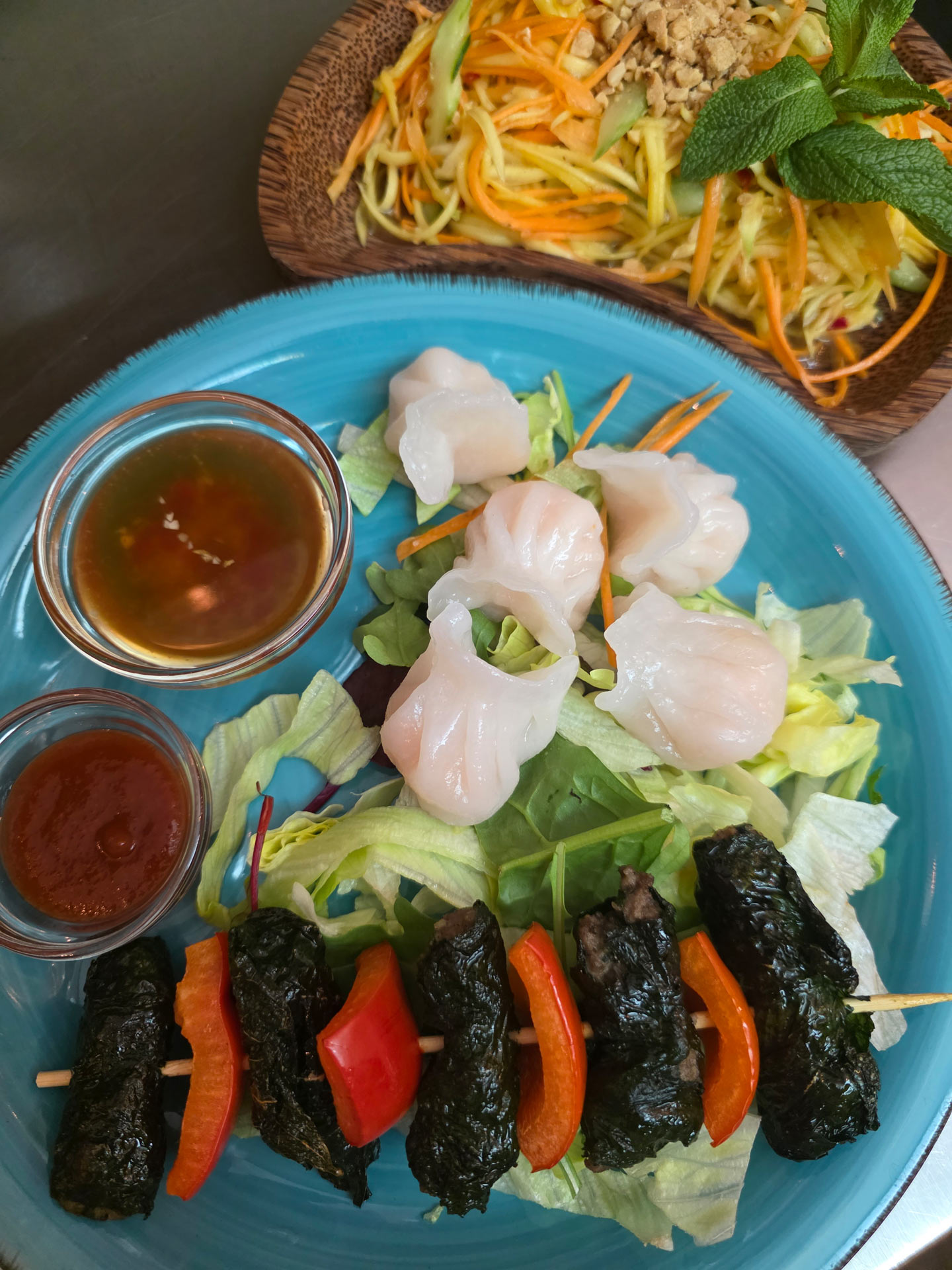 Ein Teller mit buntem asiatischem Essen, Garnelen, Sauce und knackigem Salat.